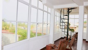 Une pièce spacieuse avec de grandes fenêtres, des chaises en bois et un escalier en colimaçon.