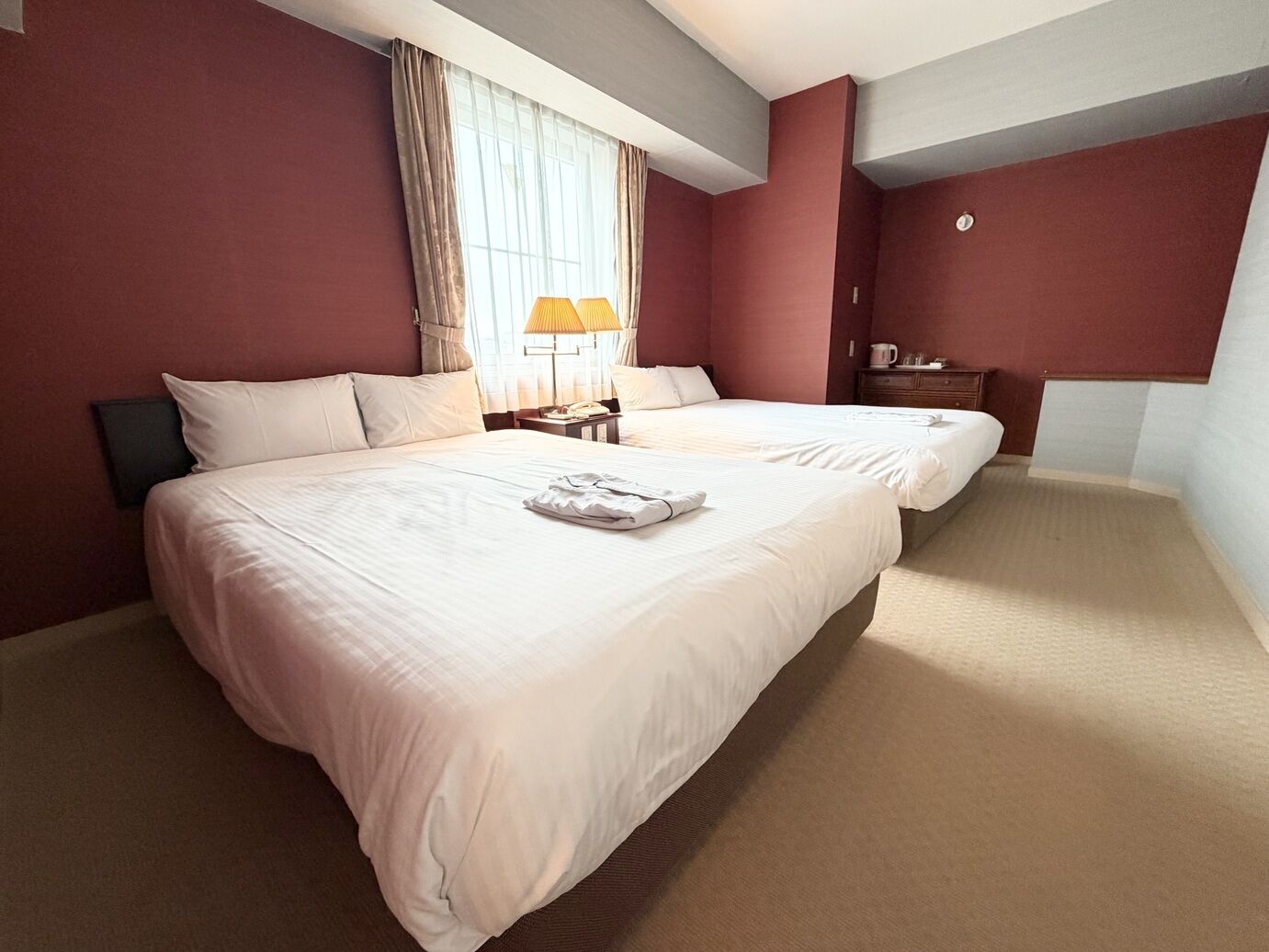 Een hotelkamer met twee bedden, een nachtkastje, een lamp en een klein tafeltje met een kop.