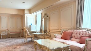 Quarto com um sofá rosa, uma mesa de centro de vidro, uma cadeira e um espelho.