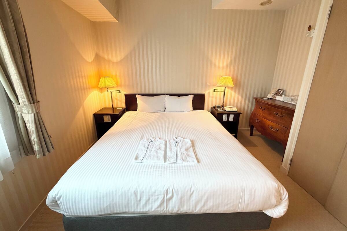 Een hotelkamer met een groot bed, twee bedlampen, een houten dressoir en een telefoon op het dressoir.