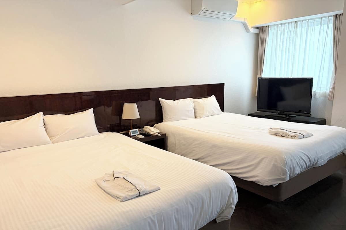 Een hotelkamer met twee bedden, een televisie en een nachtkastje met een lamp en telefoon.
