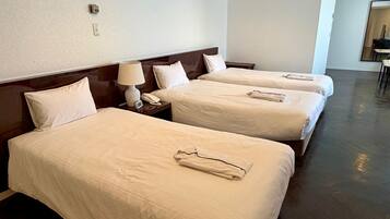 A hotel room with three beds, a bedside table with a lamp, a phone, and a small clock.