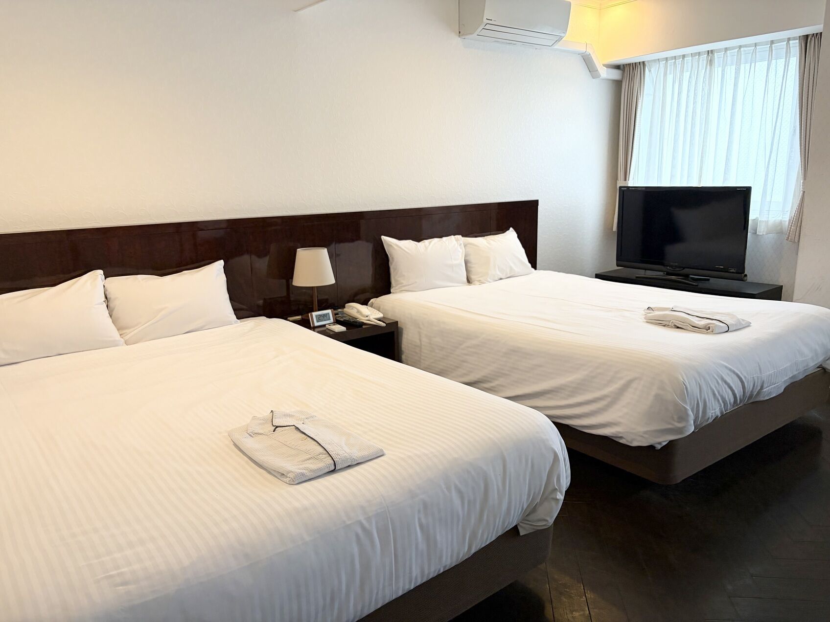 Een hotelkamer met twee bedden, een televisie, een nachtkastje met lamp en een airconditioningsunit.