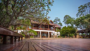 A large, two-story wooden lodge with a balcony, surrounded by lush greenery and a wooden deck. - The Log Home Experience Khao Yai (Pak Chong)