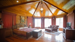 A spacious room with a large bed, a sofa, a television, and a wooden ceiling. - The Log Home Experience Khao Yai (Pak Chong)