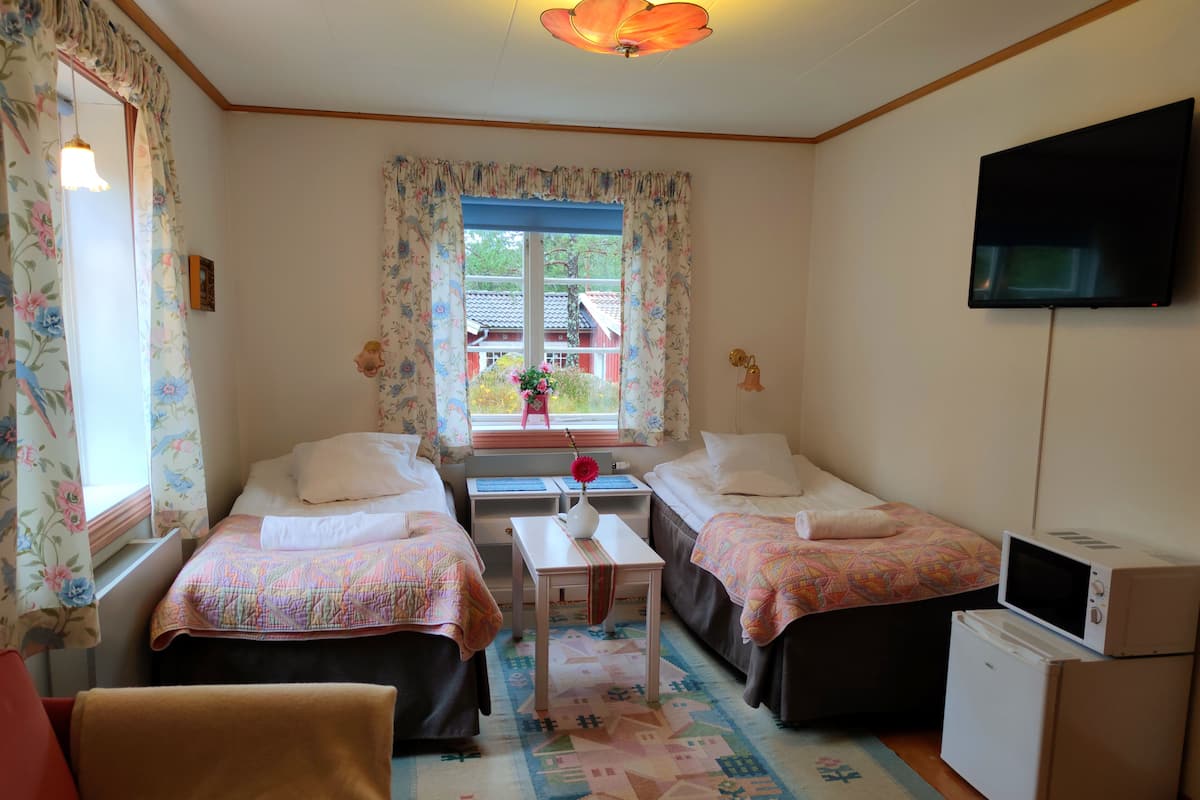 A bedroom with two beds, a small table, a TV, and a refrigerator.
