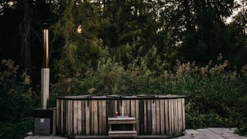 A wooden outdoor seating area with a bench and a table, surrounded by dense foliage.