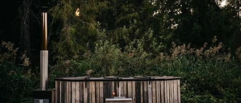Un área de estar exterior de madera con un banco y una mesa, rodeada de follaje denso.