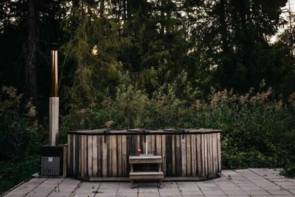 A wooden outdoor seating area with a bench and a table, surrounded by dense foliage. - Odalgården (Uppsala)
