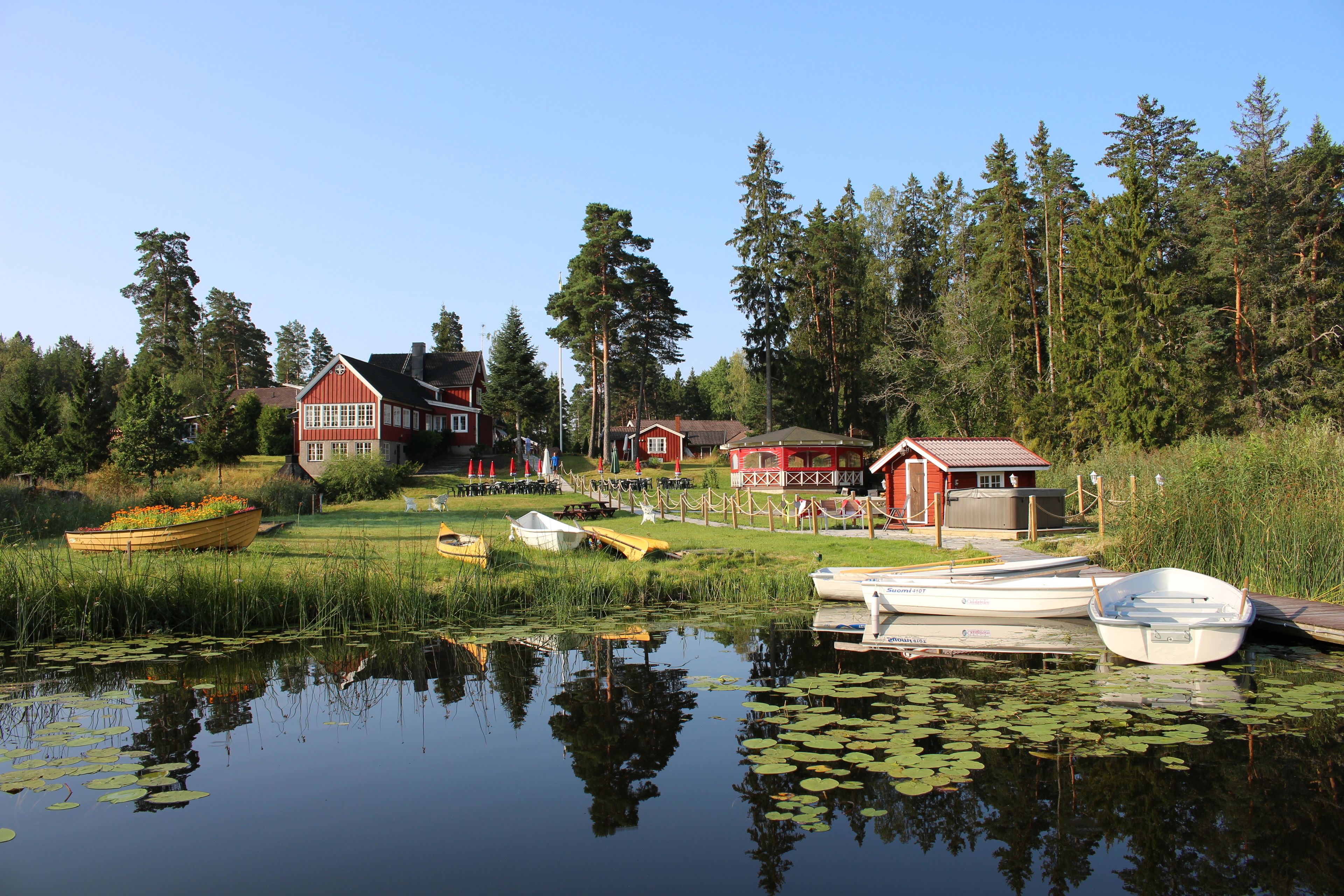 A lakeside property with boats docked, a wooden boat with flowers, and a red building.