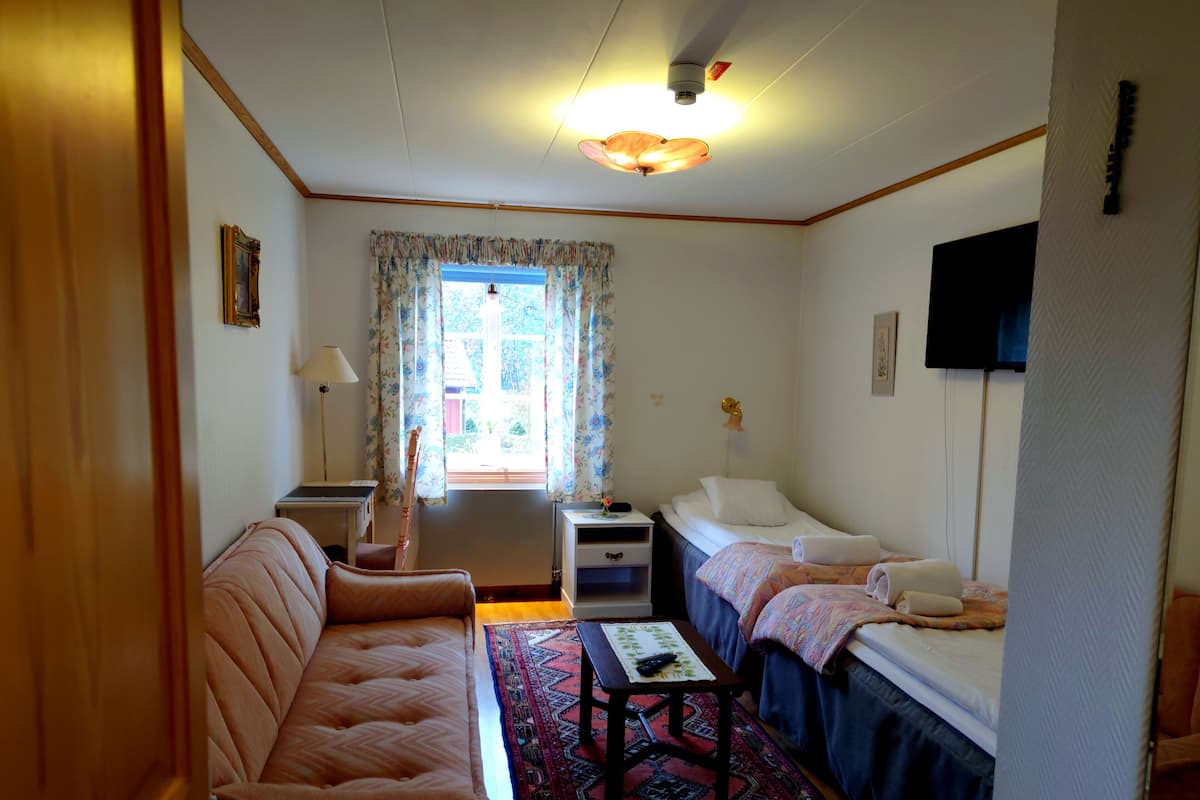 A compact hotel room with a sofa, two single beds, a small table, a TV, and a window with curtains.