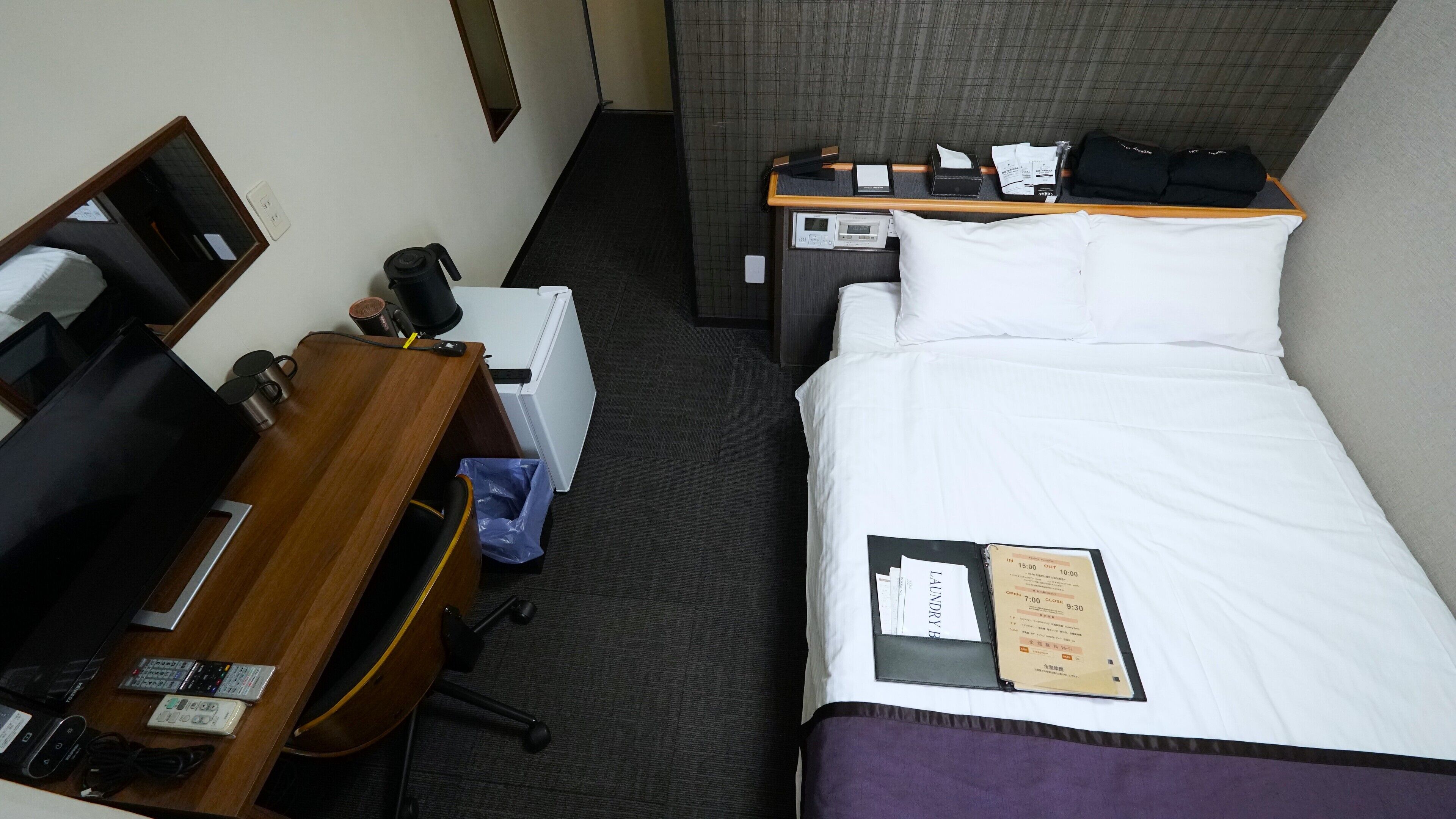 A hotel room with a bed, a desk with a computer, a telephone, and a small table with a coffee maker.