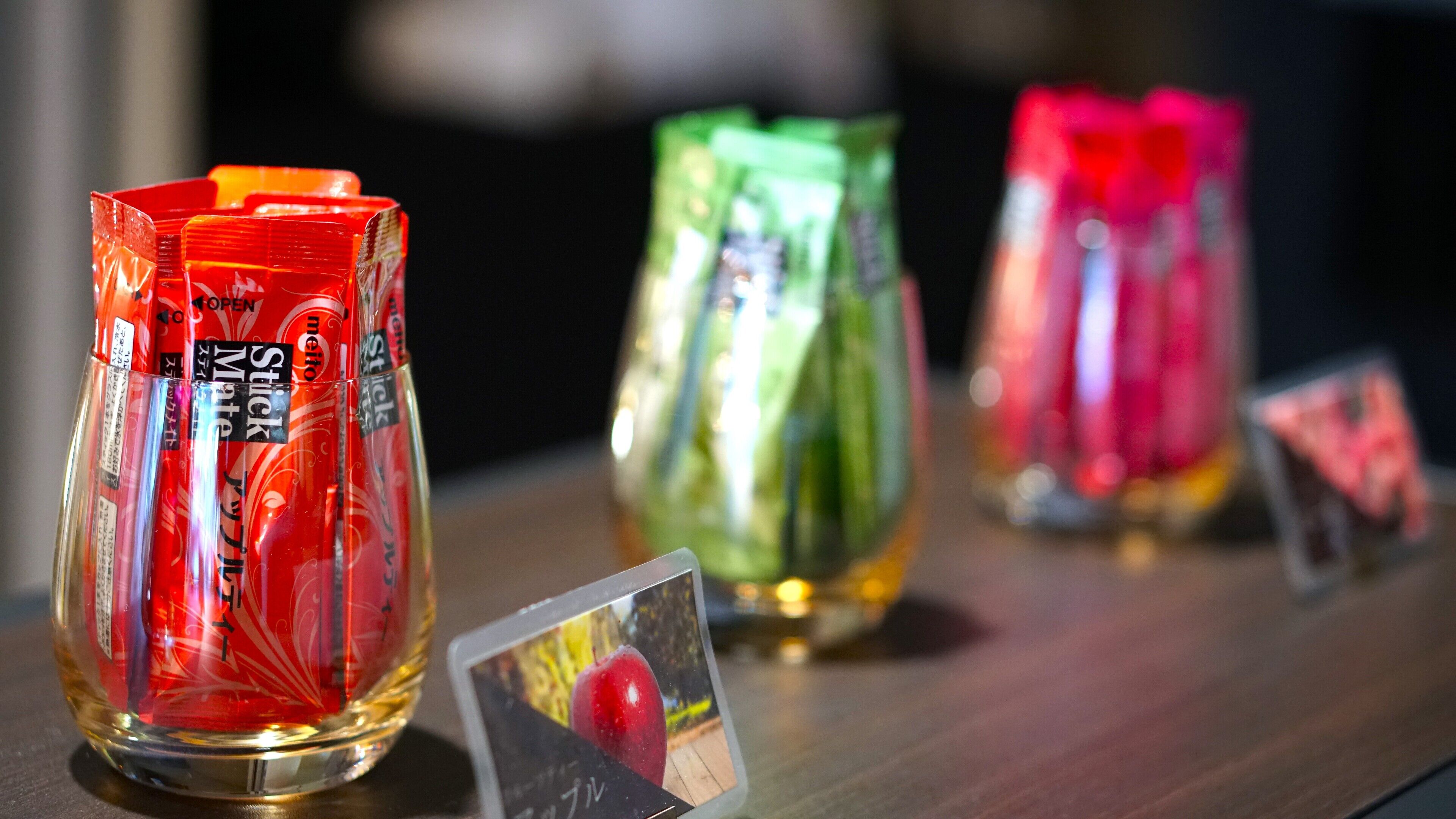 Three glass candle holders with labels on a wooden surface.
