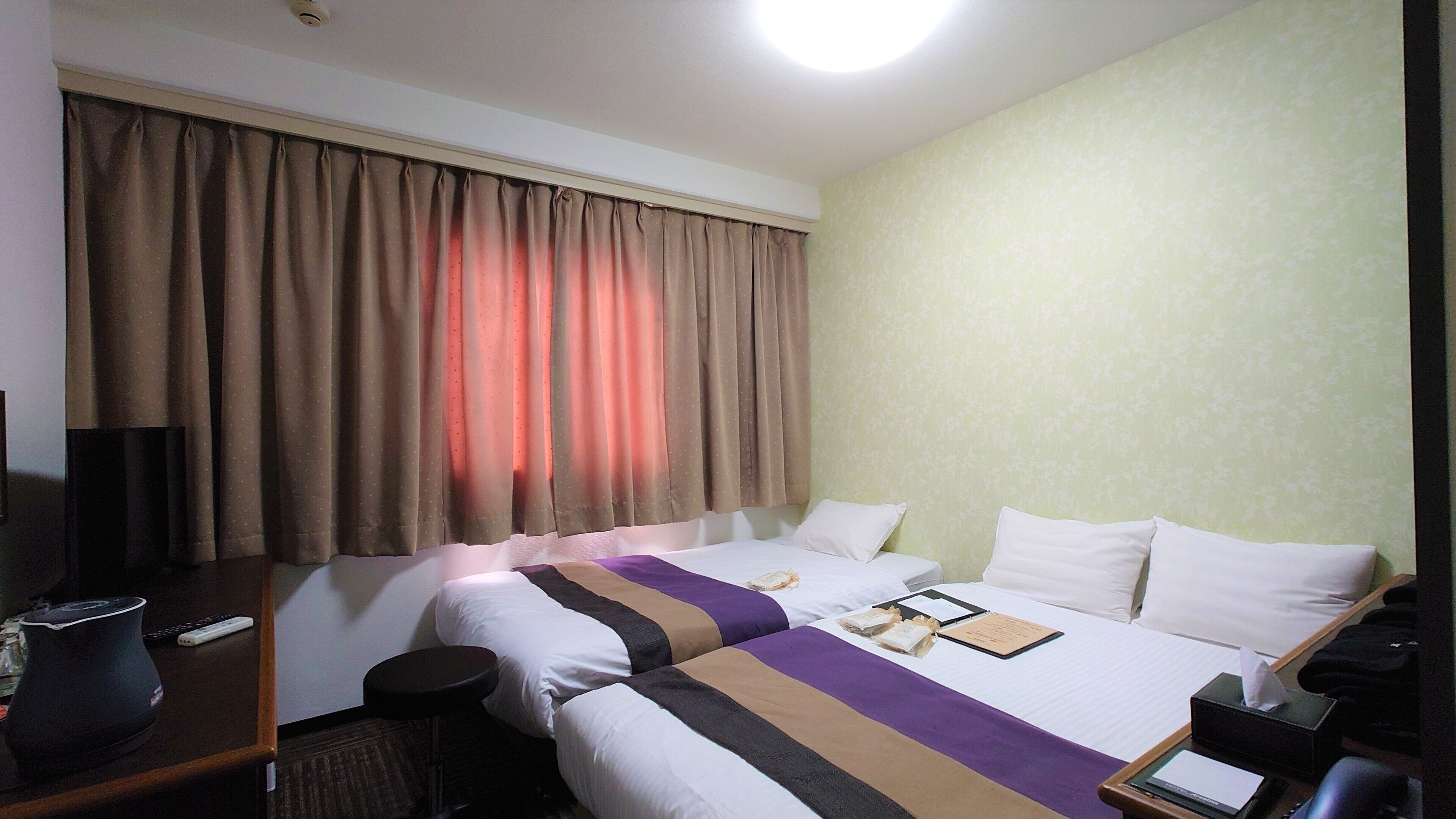A hotel room with two beds, a desk with a lamp, a TV, and a window with curtains.