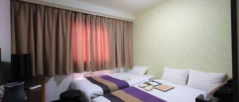 A hotel room with two beds, a desk with a lamp, a TV, and a window with curtains.