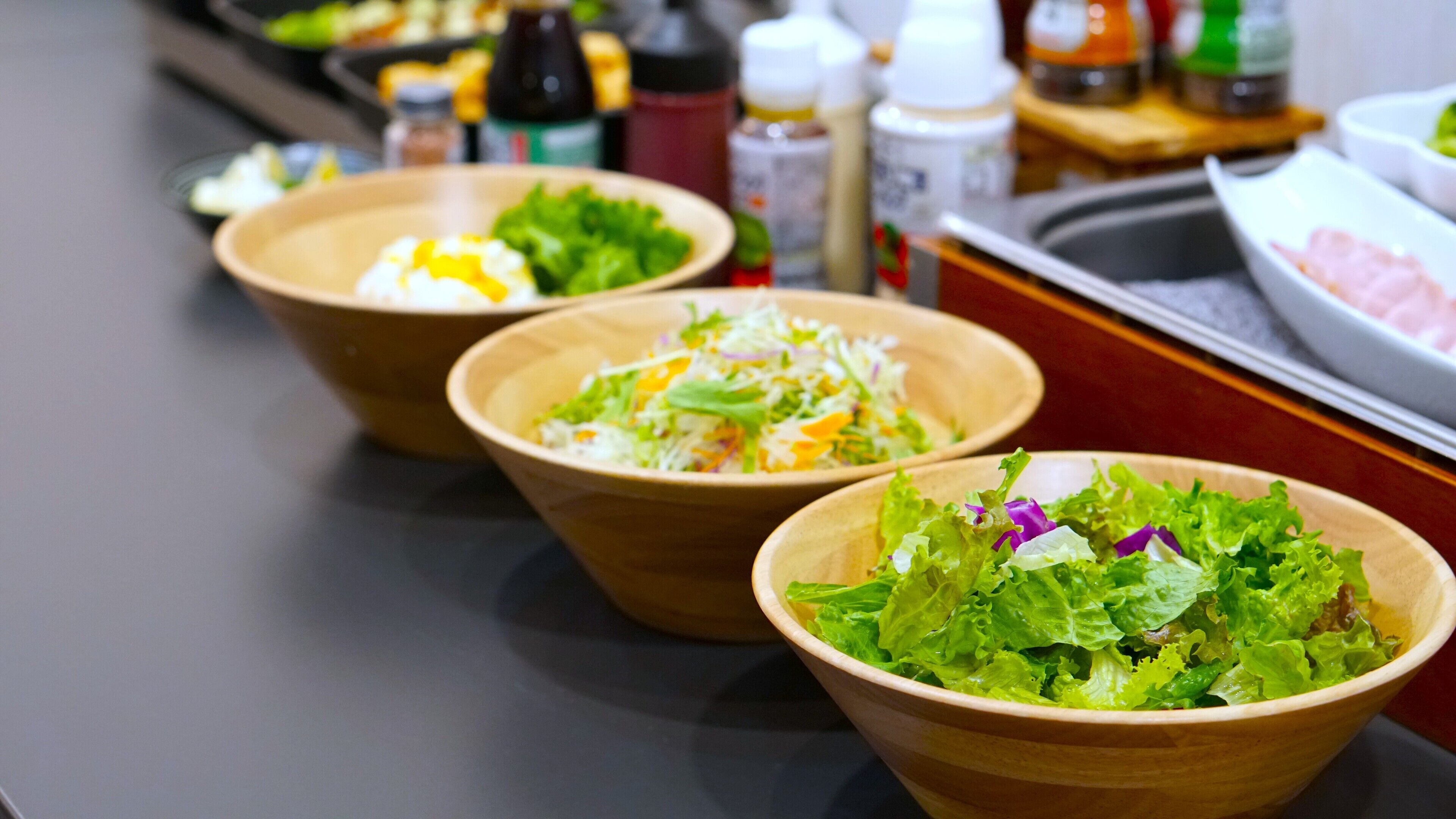 Three wooden bowls with salads on a table.