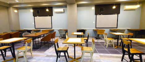 Un aula con escritorios y sillas dispuestos en filas, unidades de aire acondicionado en las paredes y una pantalla de proyector.