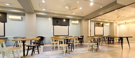 A conference room with tables and chairs, a projector screen, and ceiling fans.