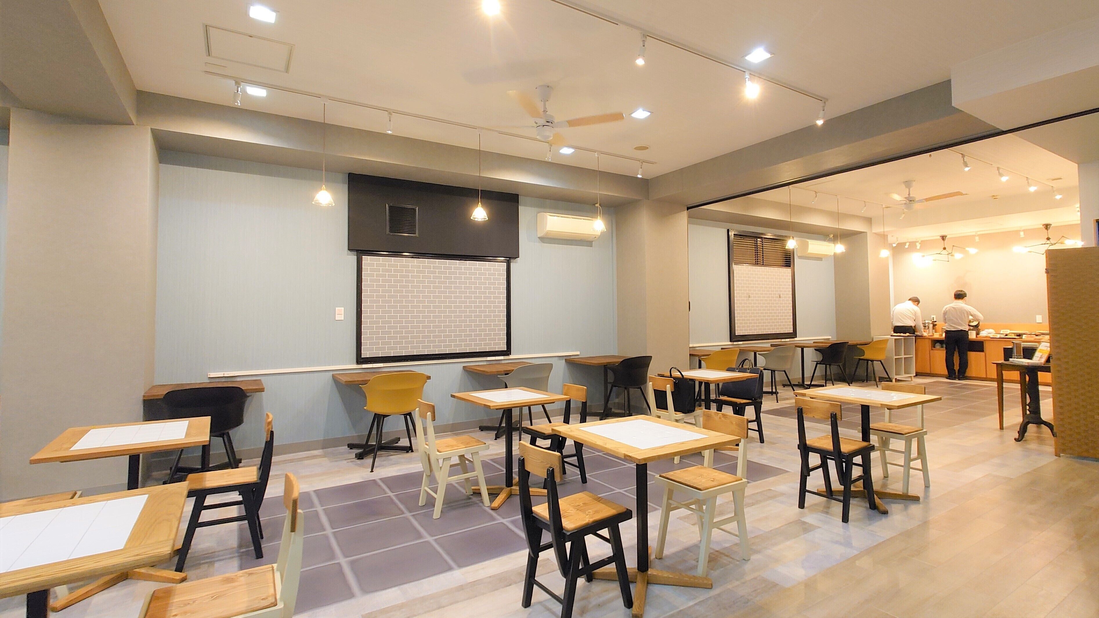 A classroom with tables and chairs, a projector screen, and a chalkboard.