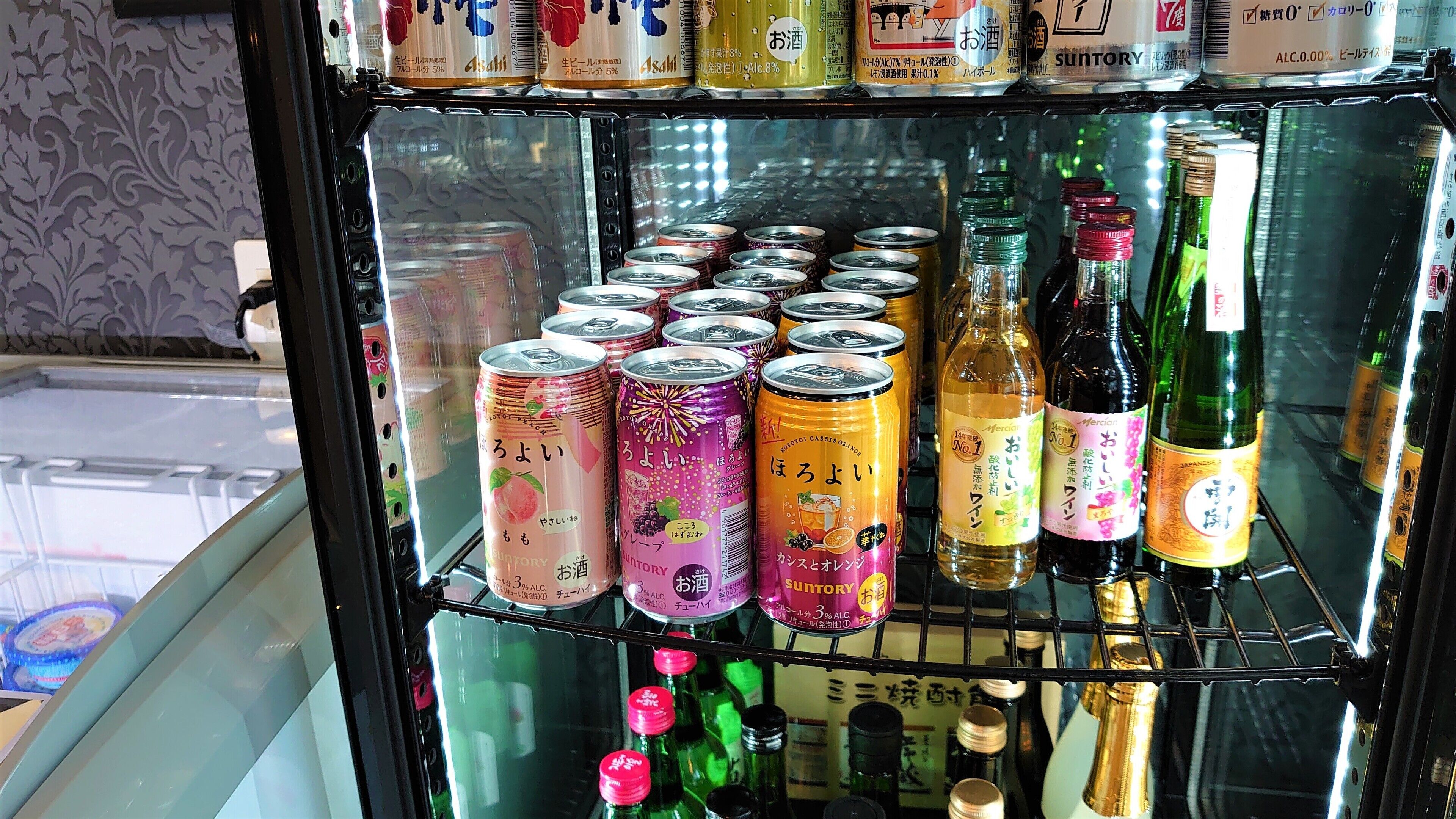 A refrigerated display case with various canned beverages and bottles, including some with Japanese labels.