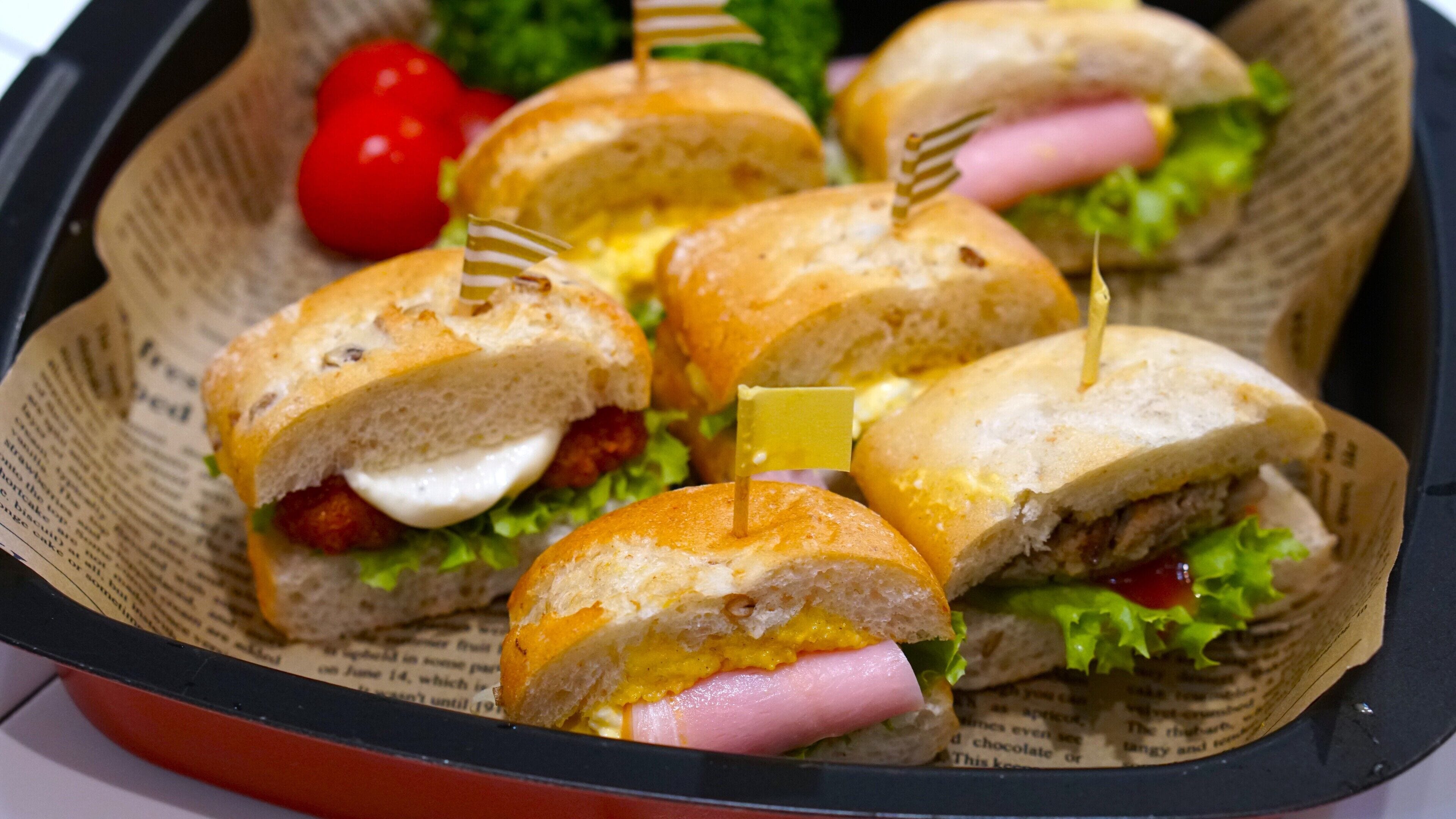 Eine Tablett mit Sandwiches, Zahnstochern, Salat und einer roten Kirschtomate.