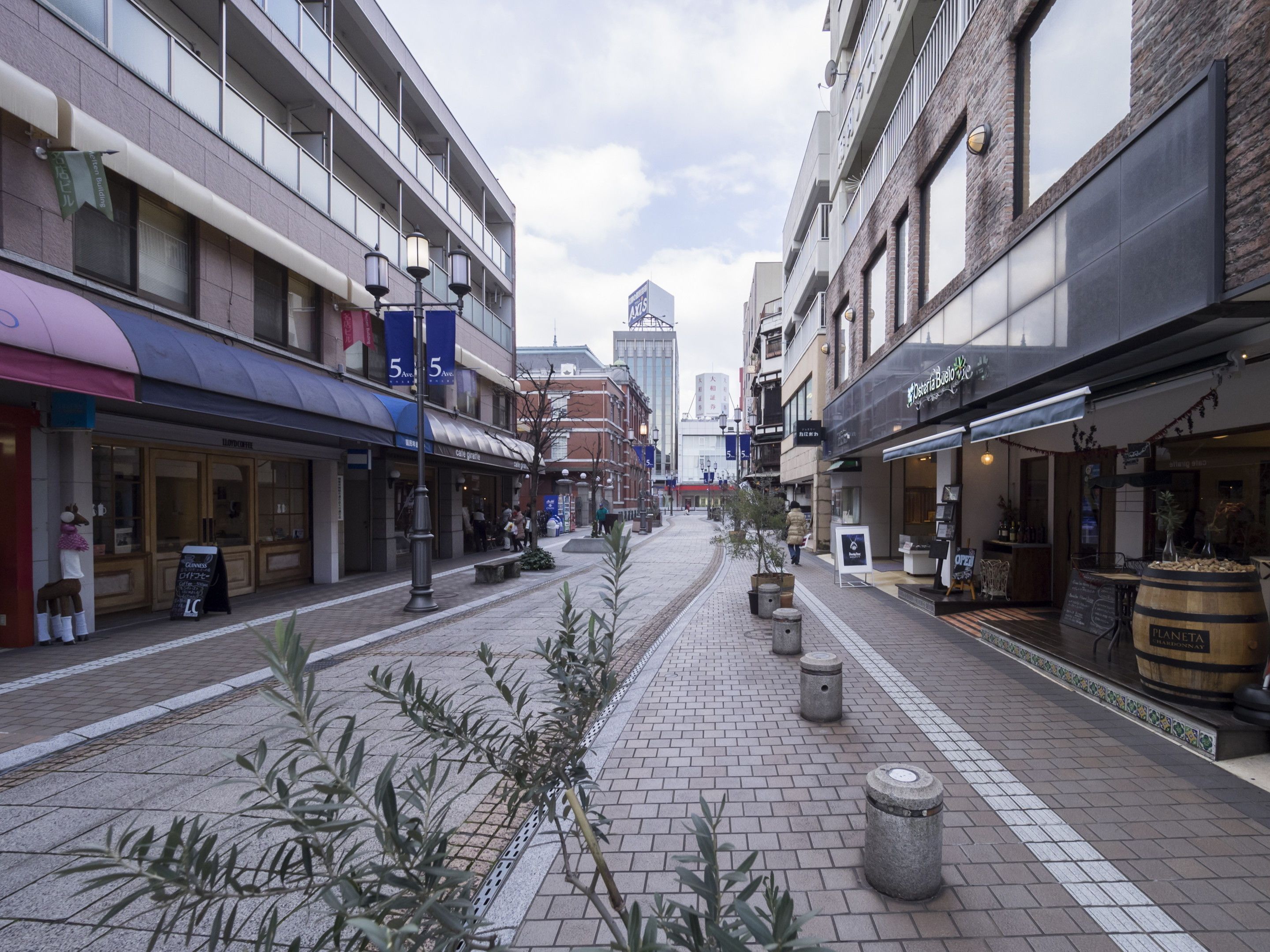 A pedestrian street lined with shops and cafes, featuring a mix of modern and traditional architecture.
