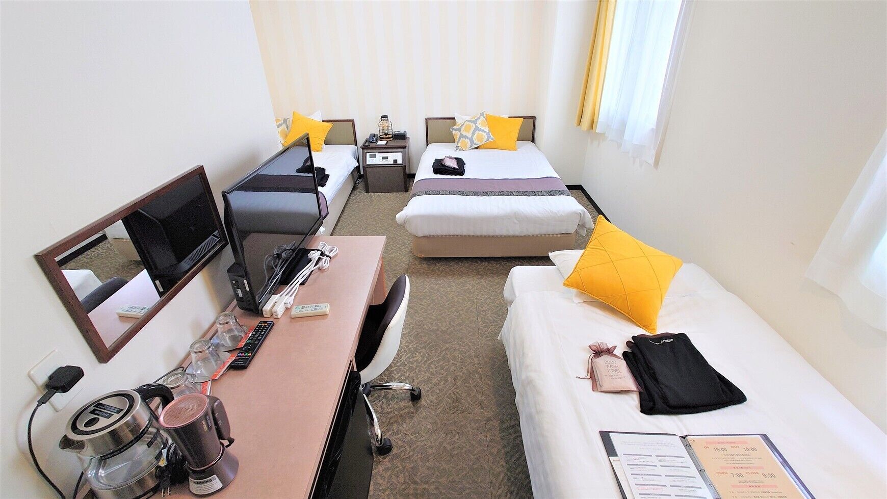 A hotel room with a desk, two beds, a TV, and a mirror.