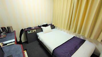 A hotel room with a bed, a desk with a telephone, a coffee maker, and a nightstand.