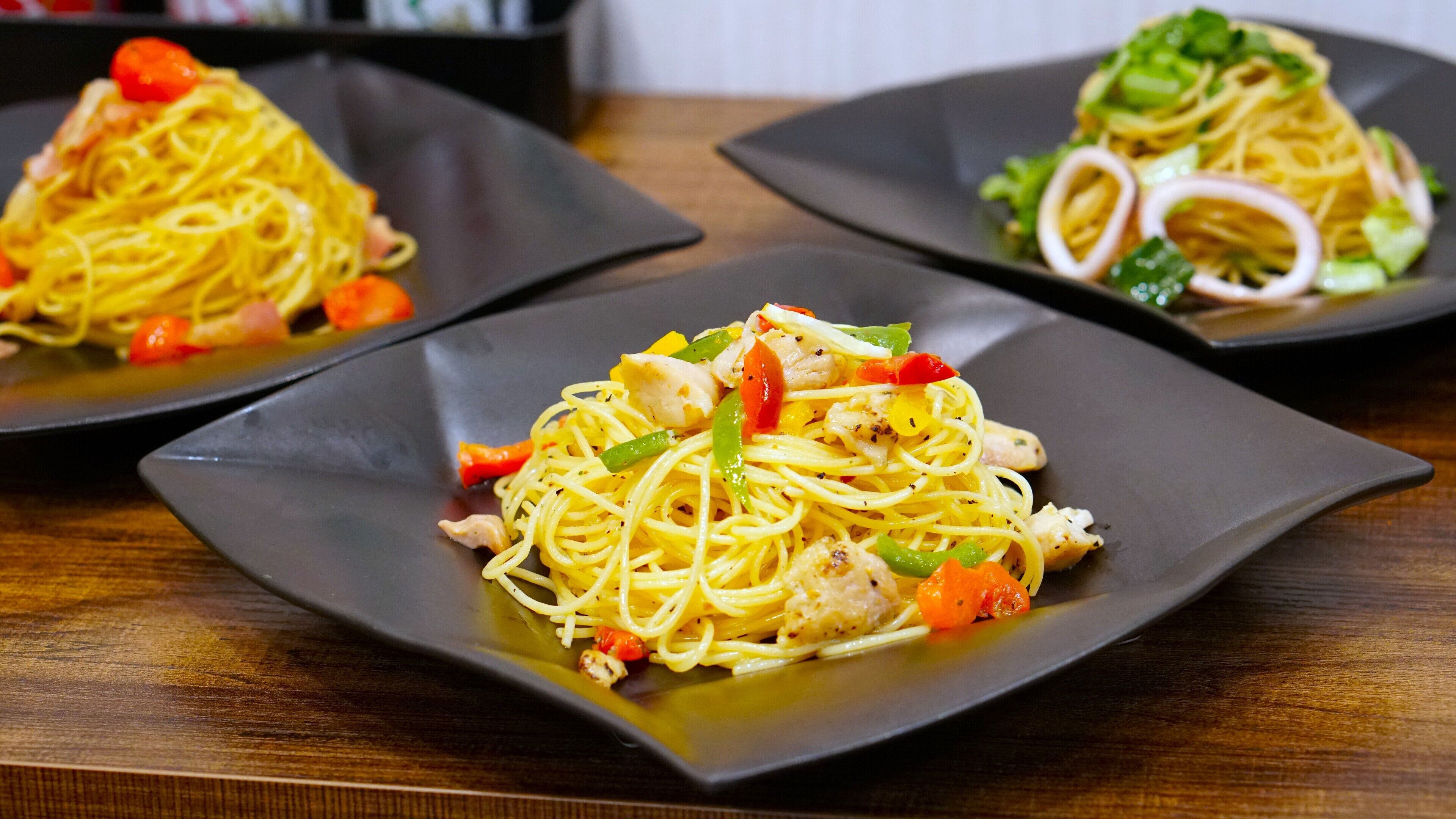 Tres plats de pasta amb verdura i pollastre sobre una taula de fusta.