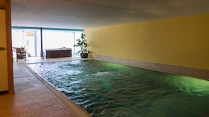 An indoor swimming pool with clear water, a tiled floor, and a yellow wall.