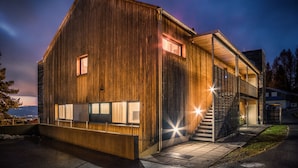 A modern building with a wooden facade, large windows, and a staircase leading to a covered entrance.