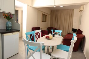 A dining area with a table, chairs, and a kitchen area with a refrigerator. - Sunquest Gardens Holiday Resort (Limassol)