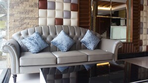A plush, tufted sofa with a cushioned backrest and armrests, positioned in front of a wall with a geometric pattern of variously hued panels. - Hatyai Holiday Hotel (Hat Yai)