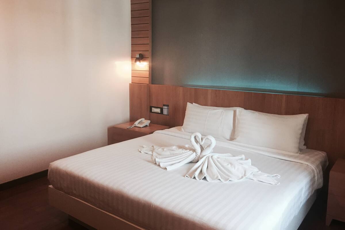 A hotel room with a neatly made bed, a bedside telephone, and a wall-mounted light fixture.