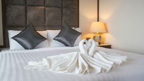 A neatly made bed with two pillows, a lamp on a bedside table, and towels arranged on the bed. - Hatyai Holiday Hotel (Hat Yai)