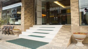 A hotel entrance with a modern design, featuring a glass facade, a set of stairs leading to the entrance, and outdoor seating with chairs and planters. - Hatyai Holiday Hotel (Hat Yai)