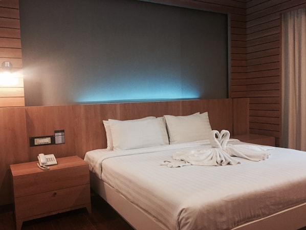Une chambre d’hôtel avec une tête de lit en bois, une table de chevet avec un téléphone et un lit bien fait, les serviettes disposées en forme de cœur.