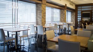 A modern dining area with glass partitions, white chairs, and a flat-screen TV mounted on the wall. - Hatyai Holiday Hotel (Hat Yai)