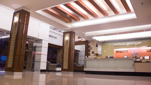 A modern hotel lobby with a reception desk, a glass partition, and a high ceiling with wooden beams. - Hatyai Holiday Hotel (Hat Yai)