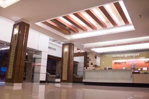 Un hall d’hôtel moderne avec un comptoir d’accueil, une cloison en verre et un plafond haut orné de poutres en bois.