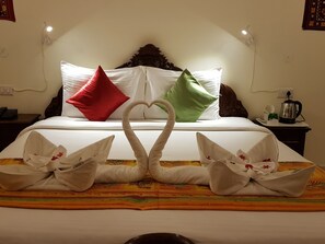 Habitación de hotel con cama, almohadas, una bandeja con tetera y una decoración de toallas con forma de cisne.