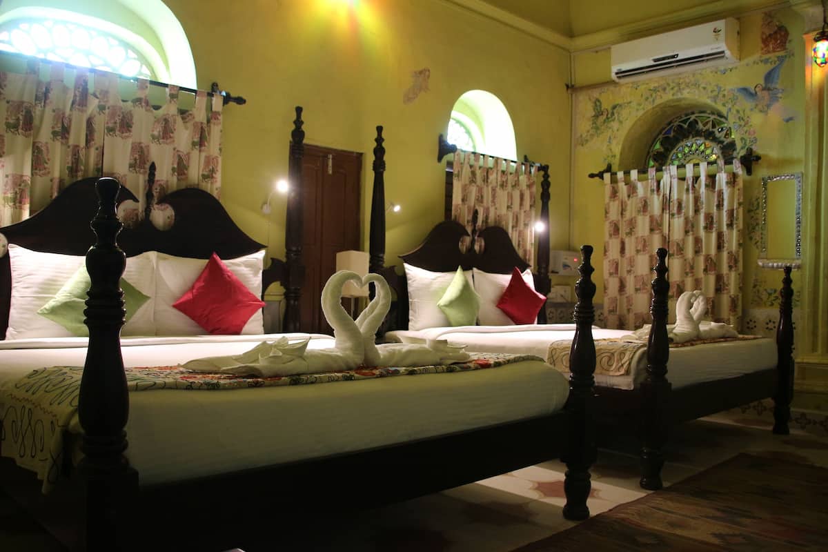 Habitación de hotel con dos camas, cada una con cabecera, y un espejo grande en la pared.