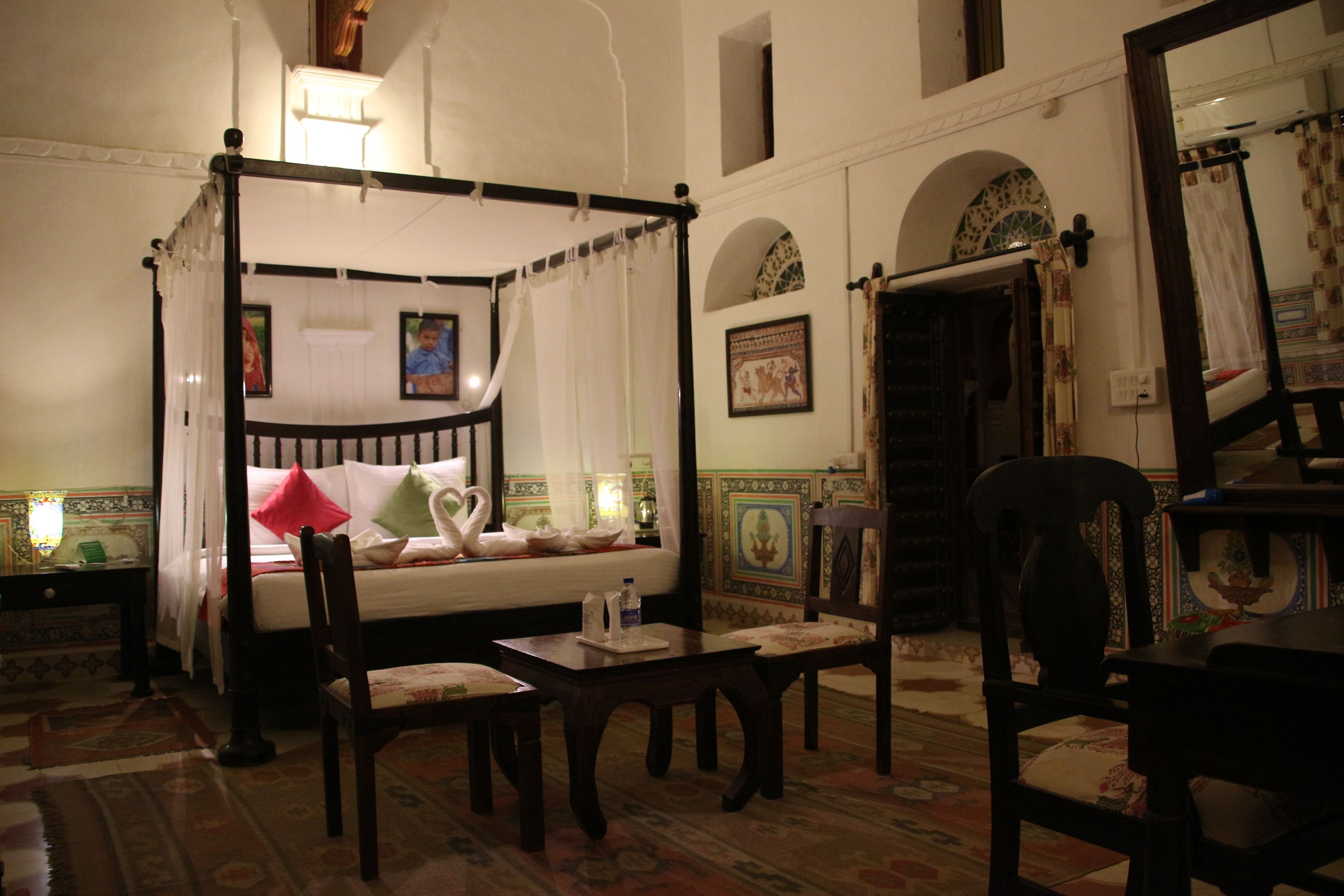 Un lit à baldaquin, une petite table, deux chaises et un miroir.
