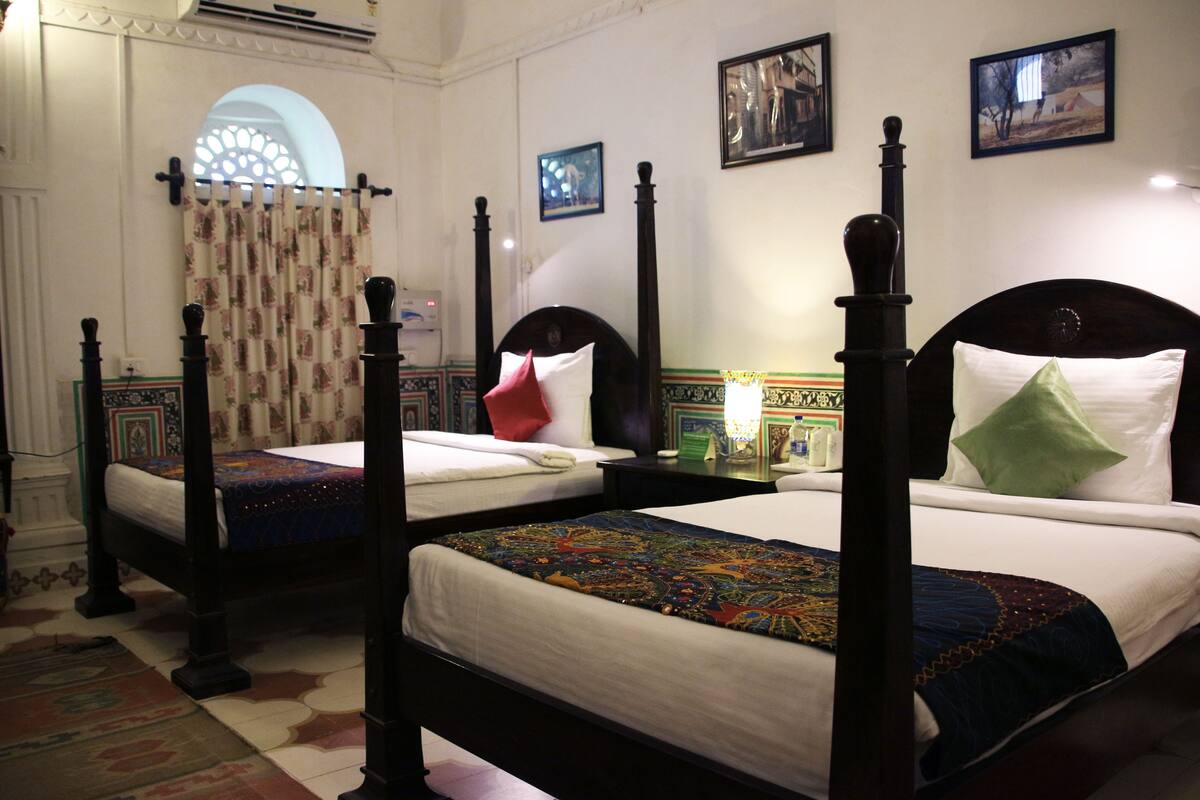 Habitación de hotel con dos camas con dosel, un ventanal con cortina decorativa y suelo de baldosas.
