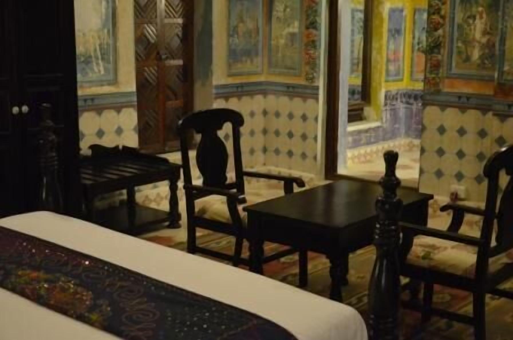 A room with a bed, two chairs, a table, and a decorative vase.