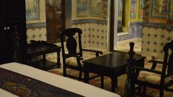 A room with a bed, two chairs, a table, and a decorative vase.