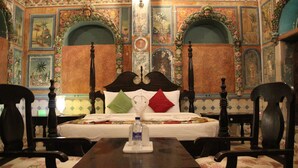 Una habitación con cama, una mesa y sillas. La habitación presenta decoraciones ornamentales y un candelabro.