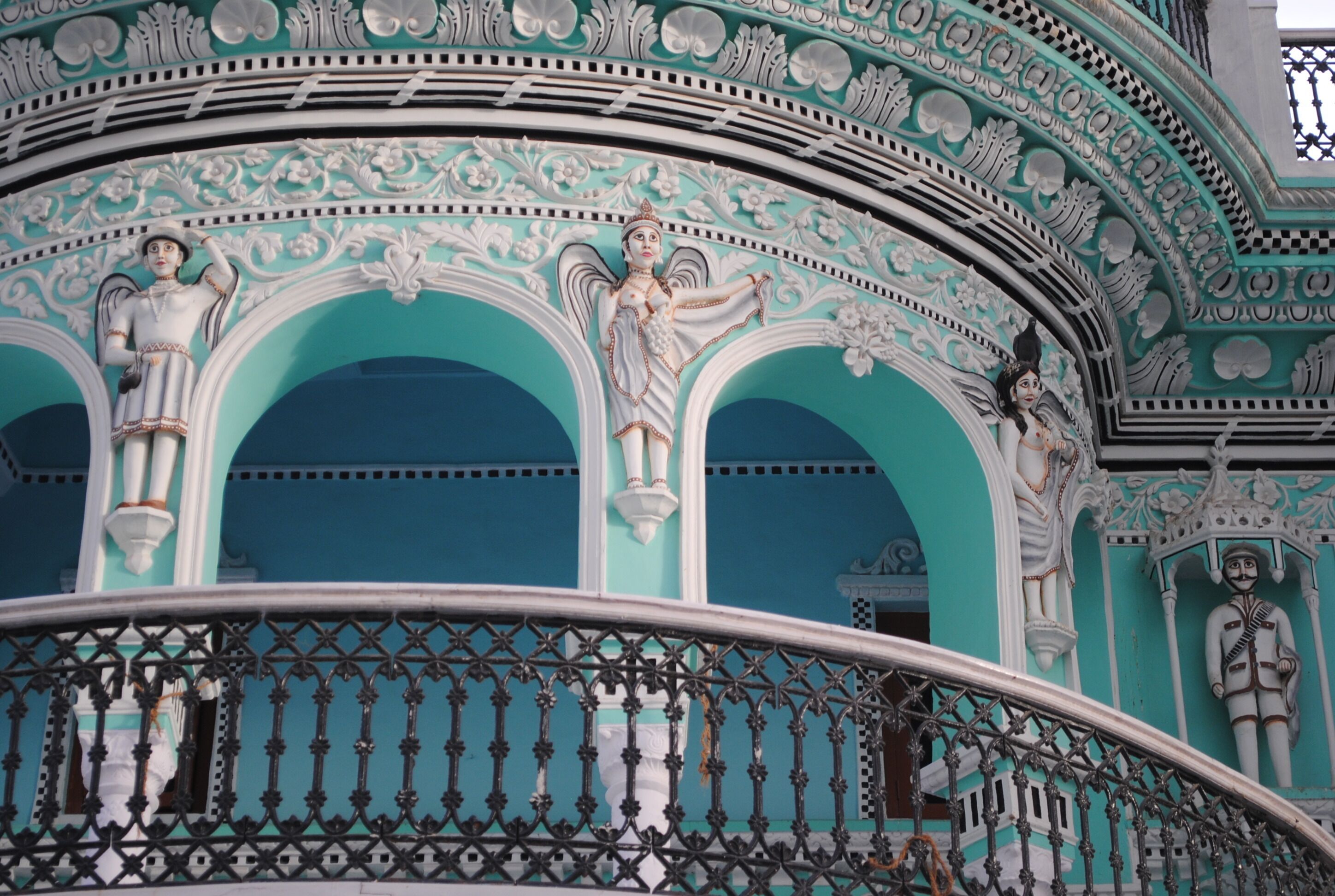 Fachada de edificio con decoraciones blancas y turquesas ornamentales, incluyendo estatuas y arcos.