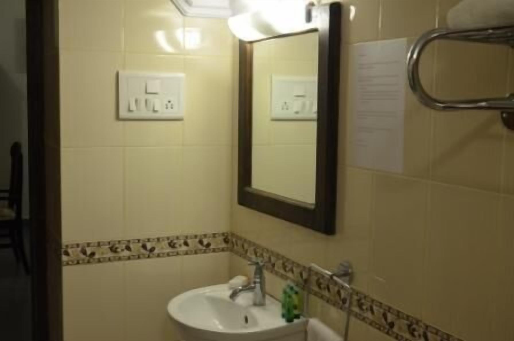 A bathroom with a sink, mirror, towel rack, and a wall-mounted light switch.