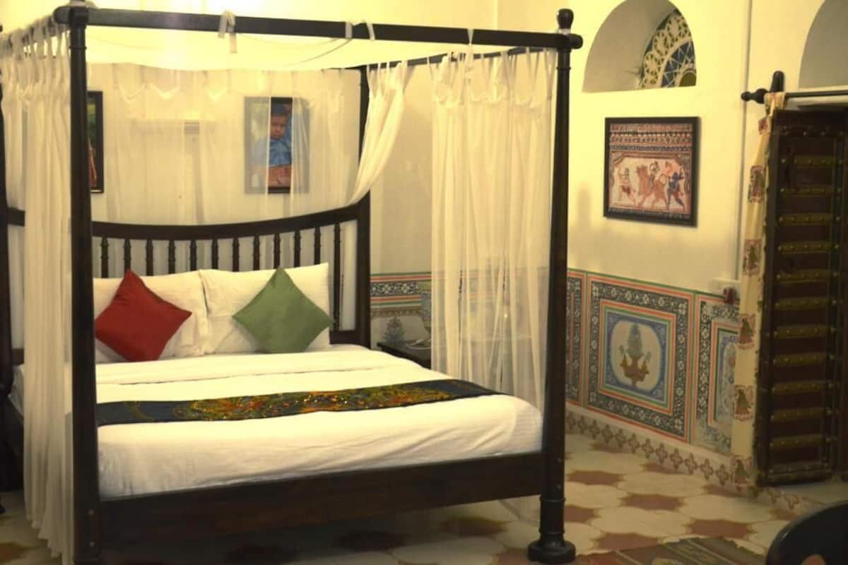Una cama con dosel y cortinas, una pared con diseños tradicionales, y una puerta con picaporte decorativo.